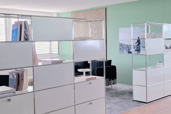 Einladend und modern gestaltetes USM-Bücherregal im Büro mit Holzpaneelen, grün-grauem Ambiente von der Natur inspiriert.