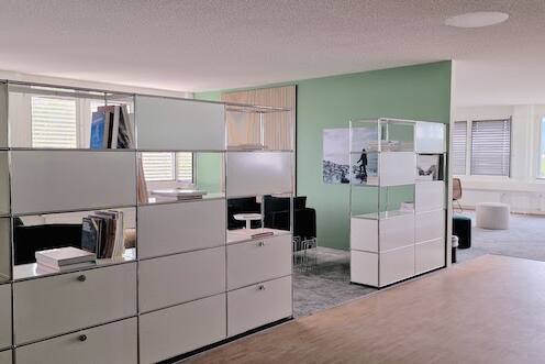 Einladend und modern gestaltetes USM-Bücherregal im Büro mit Holzpaneelen, grün-grauem Ambiente von der Natur inspiriert.