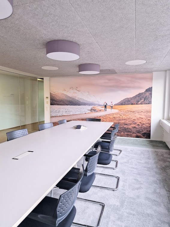 Sitzungszimmer mit XXL-Bild und grün-grauem Fliesenteppich, weisser Vitra Tisch