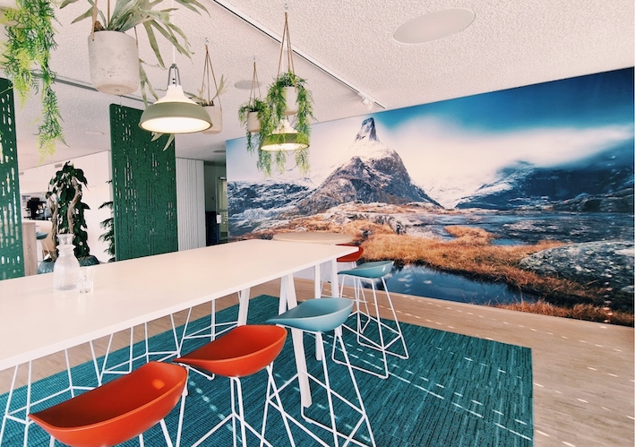 Work Café mit grossem XXL Bild und roten und blauen Hochstühlen. Kreativer Arbeitsplatz mit inspirierender Atmosphäre.